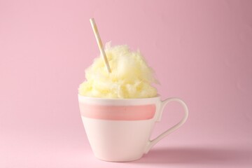 Tasty cotton candy with straw in cup on pink background