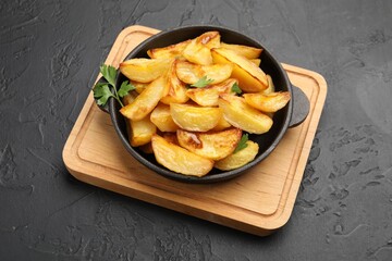 Tasty baked potatoes with parsley in frying pan on dark textured table