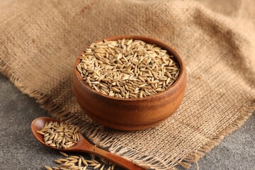 Wheat grains in bowl and spoon on grey table, closeup