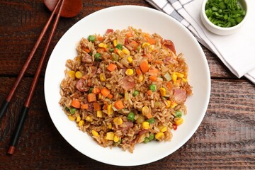 Tasty fried rice and chopsticks on wooden table, flat lay
