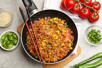 Delicious fried rice in frying pan, chopsticks and ingredients on grey textured table, flat lay