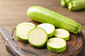 Fresh ripe zucchinis with knife on wooden table, closeup. Whole and cut