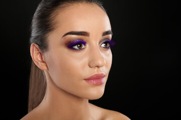 Fototapeta premium Young woman with beautiful makeup and purple eyelashes against black background, closeup