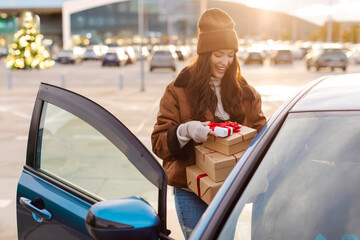 Excited woman putting Xmas gift boxes into car after shopping in mall, enjoying holidays preparation, standing at outdoor parking lot © Home-stock