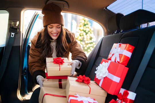 Excited woman putting wrapped Xmas gift boxes into car on back seat, preparing to deliver presents and enjoying atmosphere of winter holidays