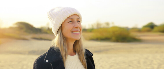 Happy stylish mature woman on coast beach, middle aged female smiling standing outdoors looking away