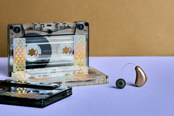Modern hearing aid beside colorful cassette tapes represents a blend of modern tech and nostalgic sounds. Audiology