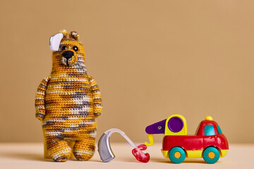 Children's audiology. Creative hearing aid for children stands next to a bright toy car and a cuddly bear, promoting sound awareness and play