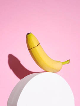 Banana with dotted line around tip balanced on white plinth