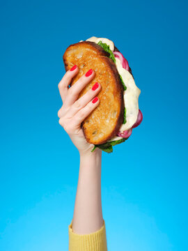 A woman's hand holding up a cheese sandwich against a blue background 