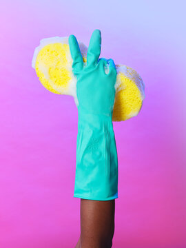 Blue rubber glove hand holding soapy sponge making rude V gesture