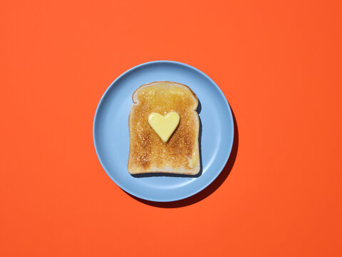 A slice of toast on blue plate with a heart shaped piece of butter on 