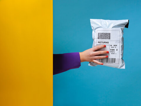 Woman&rsquo;s hand holding parcel from behind yellow wall.