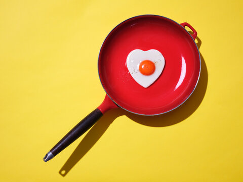 A heart shaped fried egg in a iron frying pan against yellow
