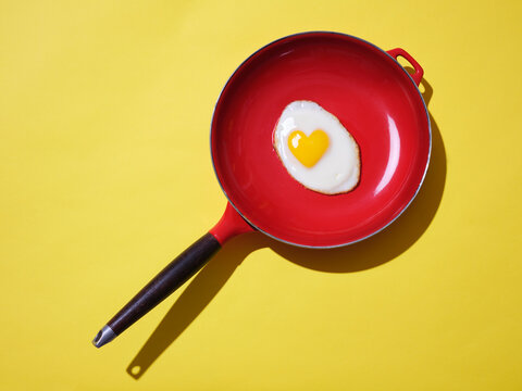 Egg with heart shaped yolk in a iron frying pan against yellow