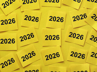 Yellow paper notes with the numbers 2026 on them stuck to a yellow background. Close up.