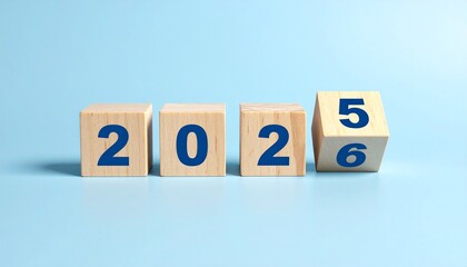 Wooden blocks displaying '2025' transitioning to '2026' with tilted final digit, arranged on light blue background in symbolic composition of time and change.
