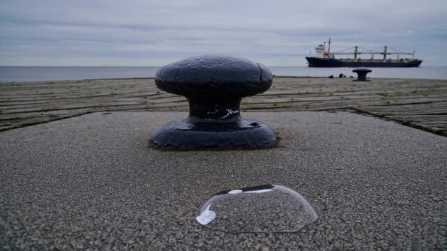 A Maritime Scene Featuring a Closeup of a Dock Cleat with a Cargo Ship on the Horizon and Safety Glasses on the Ground, Capturing a Calm Coastal Setting