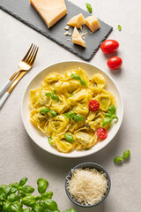 Flat lay of tortellini pasta with parmesan, pesto and basil in a plate on a light  background