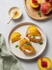 Toasted bruschetta with peach, nectarine, cream cheese or ricotta and honey on a plate on a light background