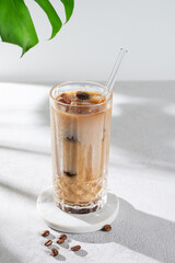 Ice latte coffee in a glass with milk and straw on a light background with coffee beans, monstera leaf