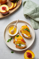 Toast bruschetta with peach, nectarine, cream cheese or ricotta and honey on a plate on a light background