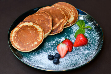 Pancakes with fresh berries and sugar powder on a black background