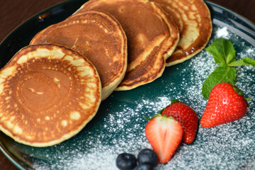 Pancakes with fresh berries and sugar powder on a black background