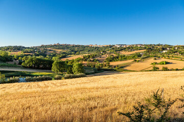 Countryside landscape with a harvested golden field in the foreground and a view of the city of...