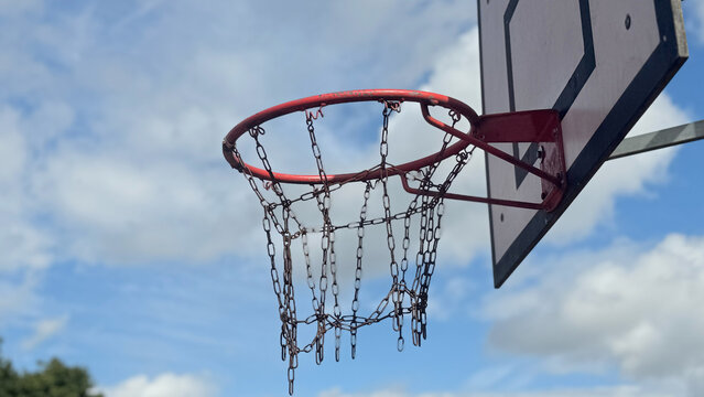 Close-up of outdoor basketball hoop with metal chain net against blue sky, suitable for topics about sports, school activities, and healthy lifestyle