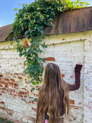 girl standing near old brick wall twined with hops