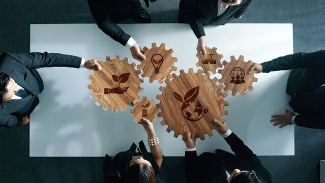 A professional team engages in a collaborative business meeting focused on sustainability, represented by wooden gears with eco-friendly symbols, fostering innovative solutions. Amity