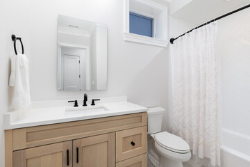 A bathroom with a white oak cabinet, black faucet on a white marble countertop, and white herringbone tile shower.