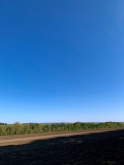 Wide rural landscape with burnt soil in the foreground, green fields and hills under a clear blue sky. Concept of agriculture, nature, and ecological contrast.