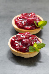 Two Cherry tartlets. With custard and mint. Dark gray background. Close up	