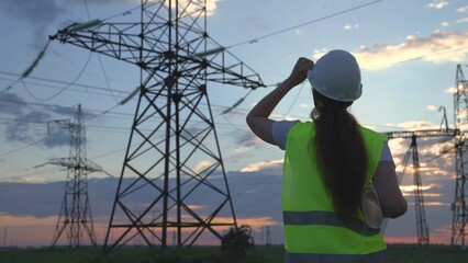 An electrician on the background of high towers of power plants looks at the project for the development of an electrical structure, the expansion of the electrical voltage of volts in the wires.