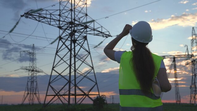 An electrician on the background of high towers of power plants looks at the project for the development of an electrical structure, the expansion of the electrical voltage of volts in the wires.
