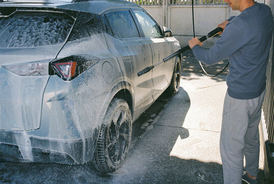 A middle-aged man washes his car at a self-service car wash.