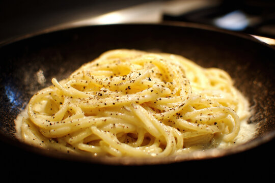 Creamy cacio e pepe pasta with freshly ground black pepper in a skillet