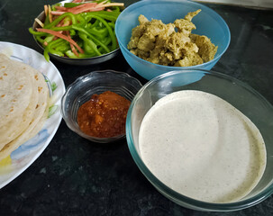 Homemade Indian meal with chapati, chutney, creamy sauce, stir-fried veggies, and spiced curry served in bowls, showcasing a wholesome traditional platter.