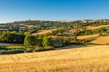 Countryside landscape with a harvested golden field in the foreground and a view of the city of...
