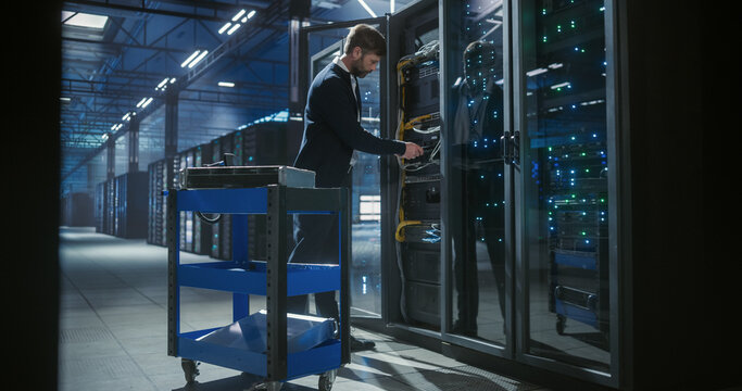 Technician checks hdd status in data cetner. Stands near hardware cart