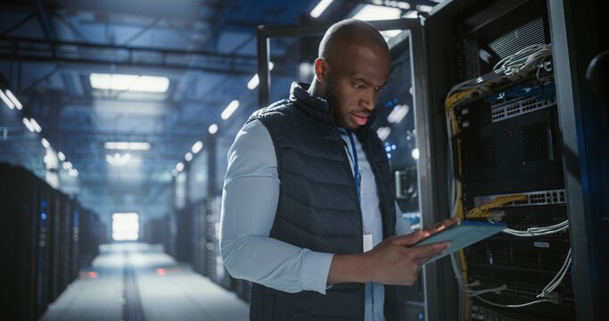 Data center technician inspects server racks, checks network cables.