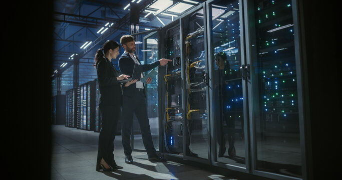 Wide view of technicians talking, using laptop and working in data cen