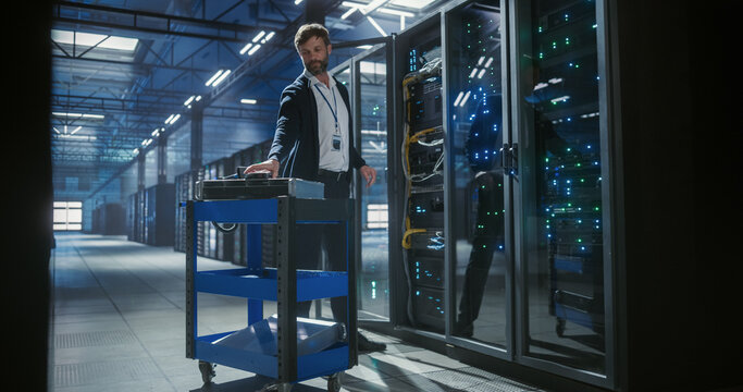 Technician checks hdd status in data cetner. Stands near hardware cart