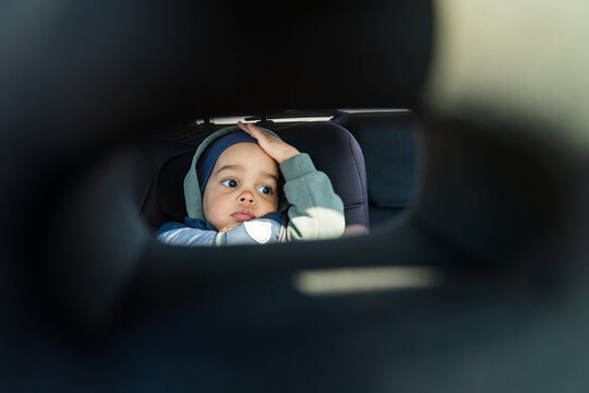 Child resting hand on head while sitting in car seat