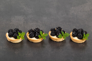 Small blackberry tartlets. With custard. Dark background. Copy space