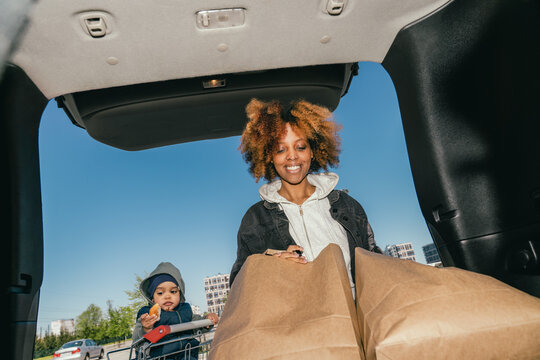 Mother loading groceries while child eats in shopping cart