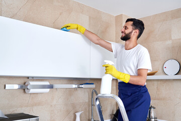 Man cleaning kitchen surface high up standing on a ladder. Cleaning service concept