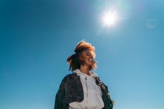 Smiling woman looking up under bright sun and blue sky